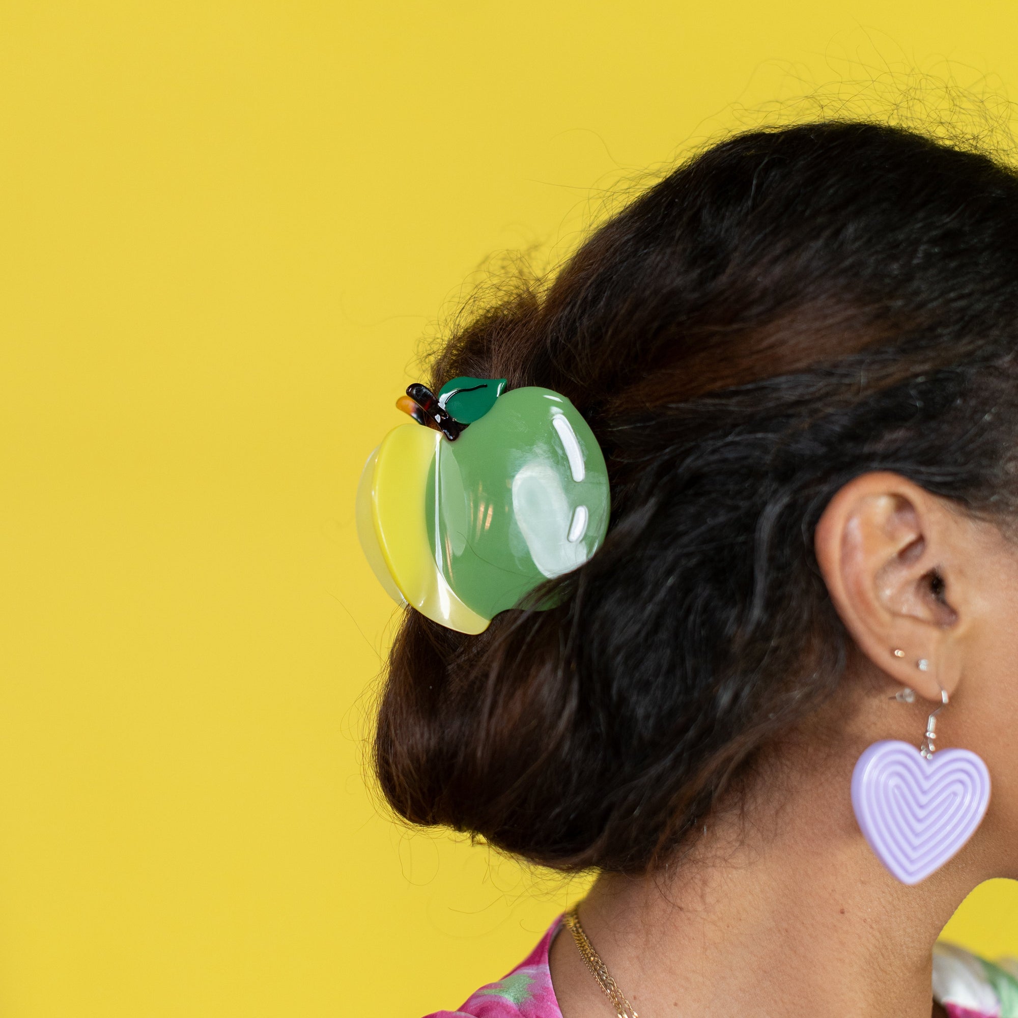 Person with colorful hair clip and heart-shaped earrings against a yellow background