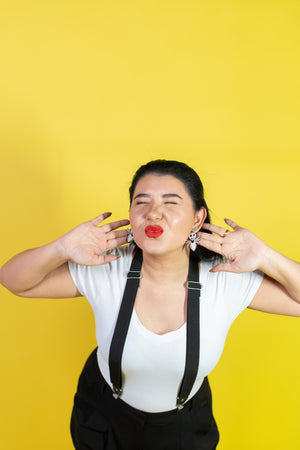 Person wearing a white shirt and black suspenders against a yellow background