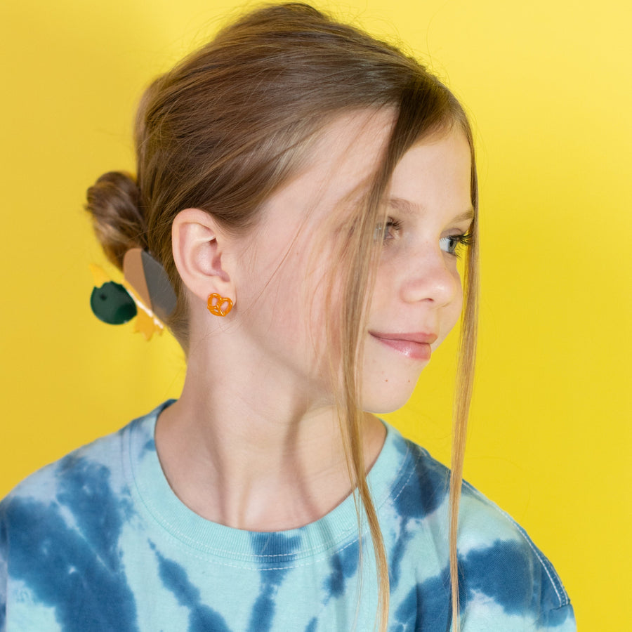 Close-up of a person wearing orange heart-shaped earrings against a yellow background