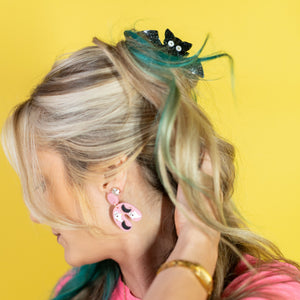 Woman with pink hair styled with a green scrunchie against a yellow background