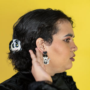 Person wearing black earrings with panda design against a yellow background