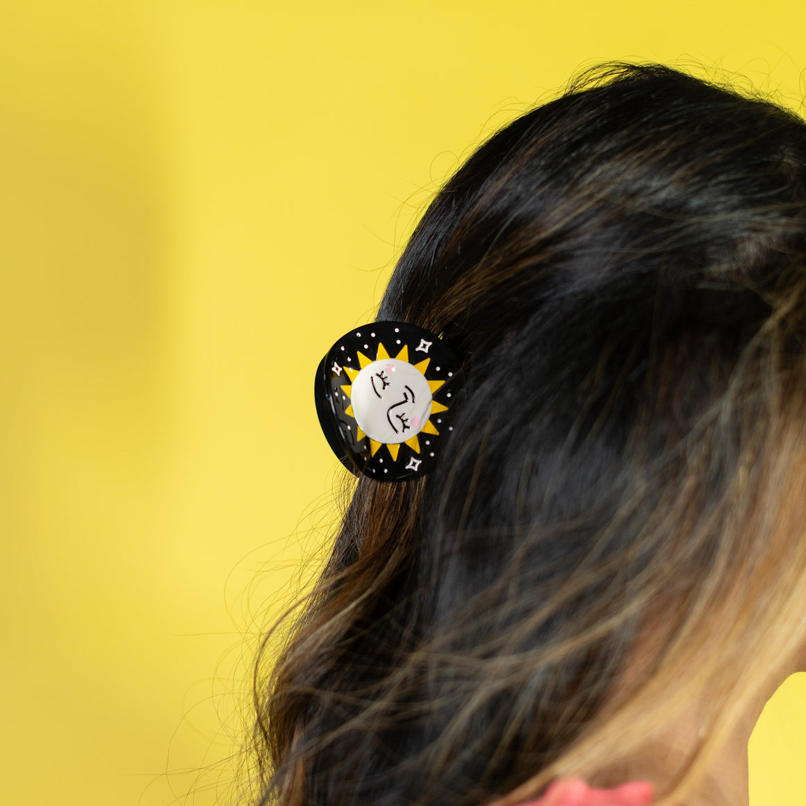 Person with a hair clip featuring a sun design against a yellow background