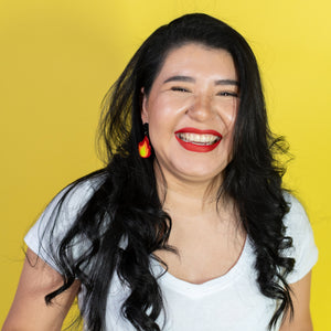 Woman with long dark hair and red lipstick smiling against a yellow background