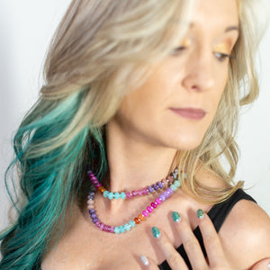 Woman with colorful hair and jewelry, wearing a black top against a white background