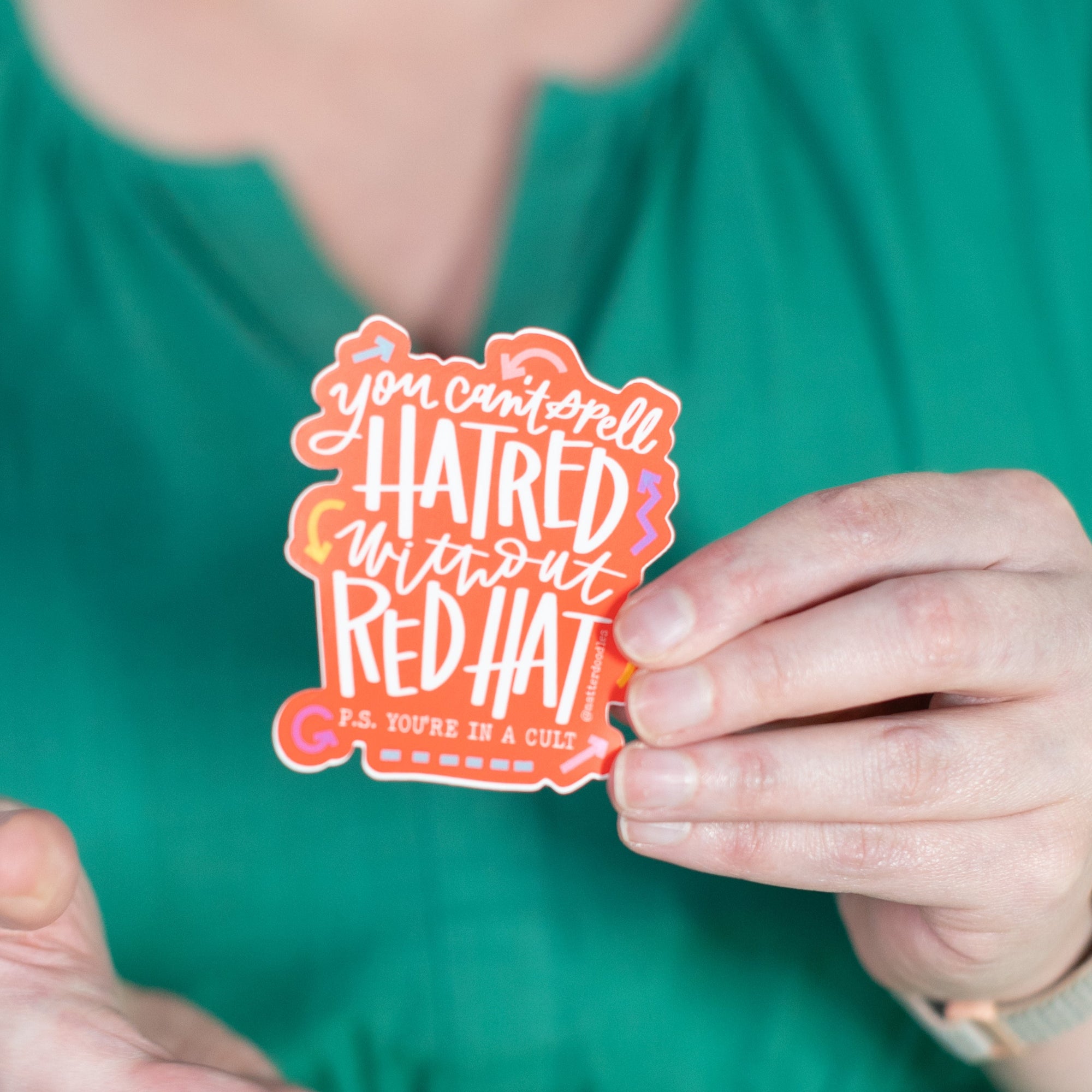 Person holding a colorful sticker with text against a plain background