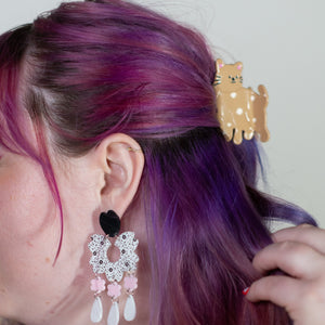 Person with purple hair styled in a ponytail, wearing a gold hair clip and earrings.