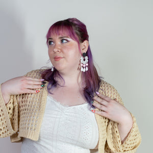 Woman with purple hair wearing a yellow cardigan and pink skirt against a plain background