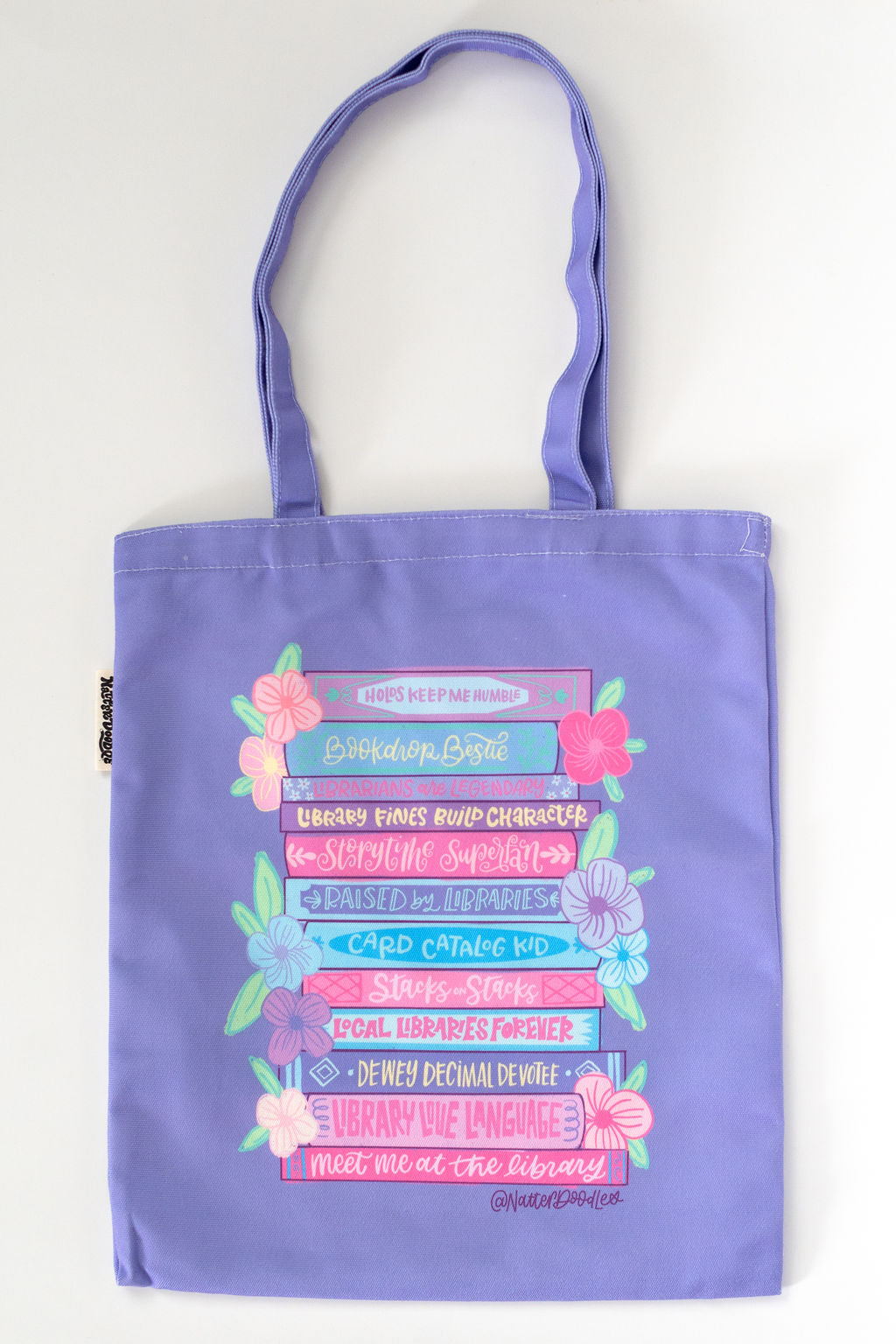 Purple tote bag with colorful text and floral designs on a white background