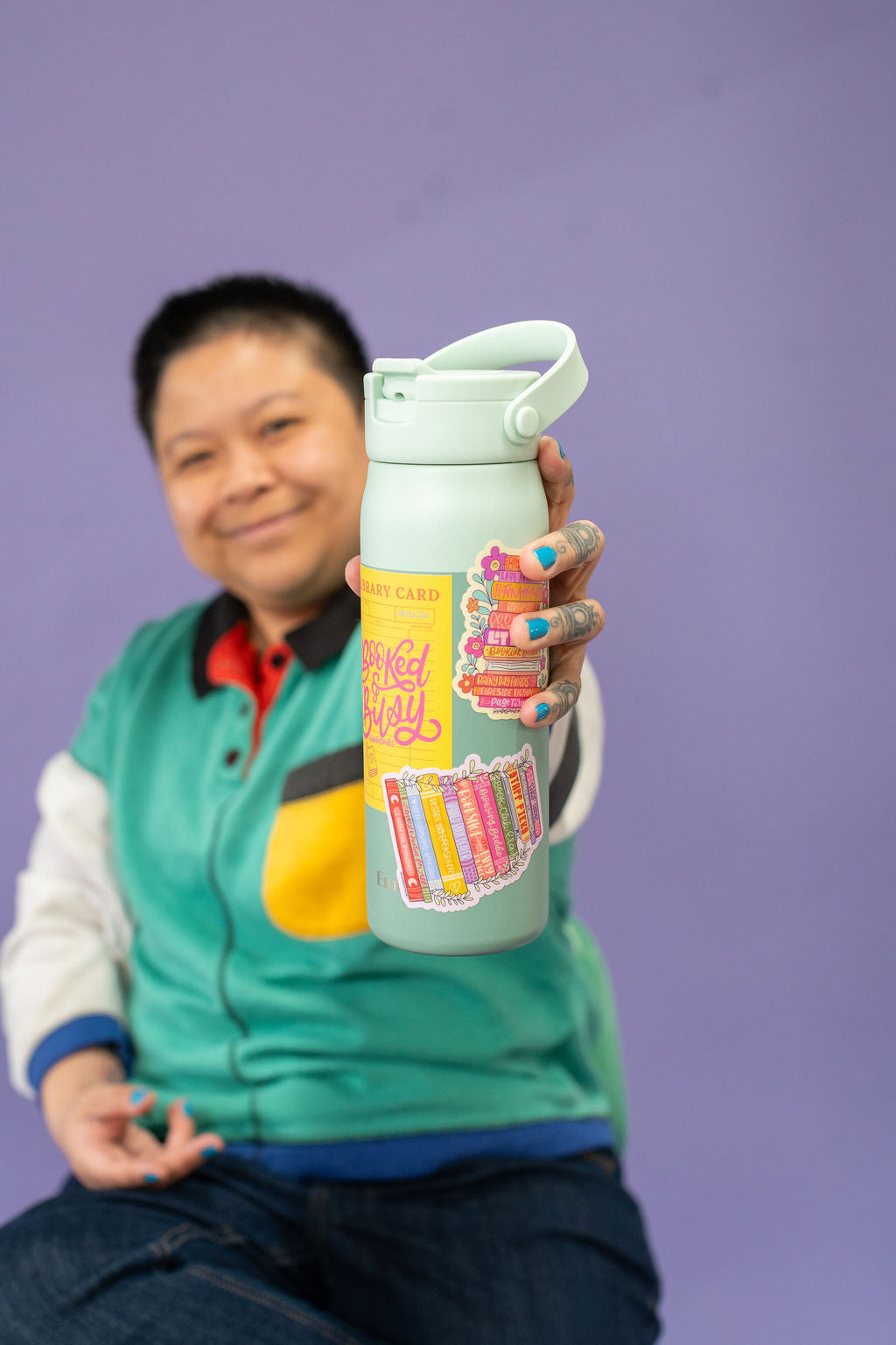 Person holding a colorful water bottle with a purple background