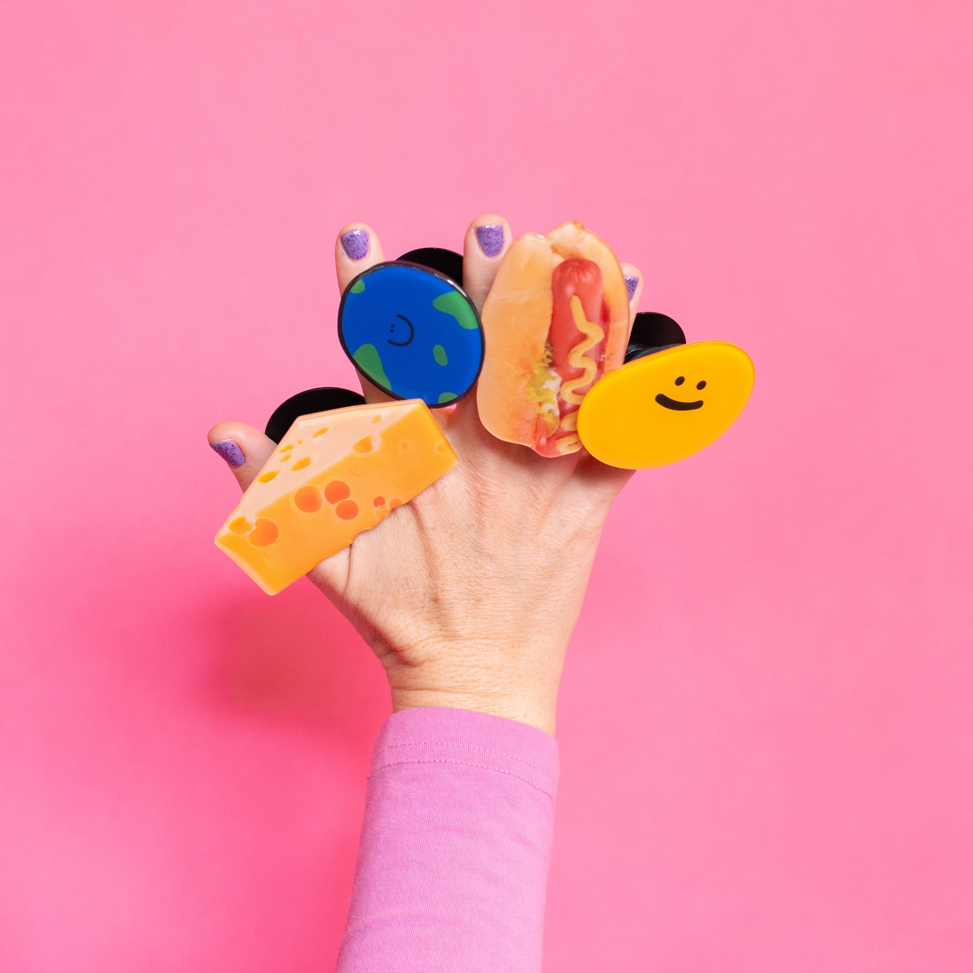 Hand holding colorful ear-shaped accessories against a pink background