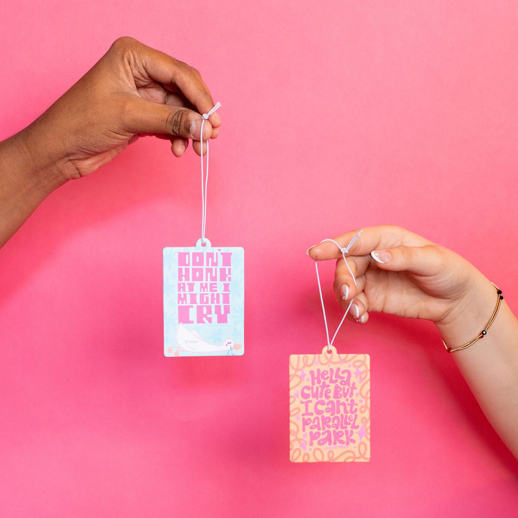 Two hands holding up two rectangular tags with text against a pink background