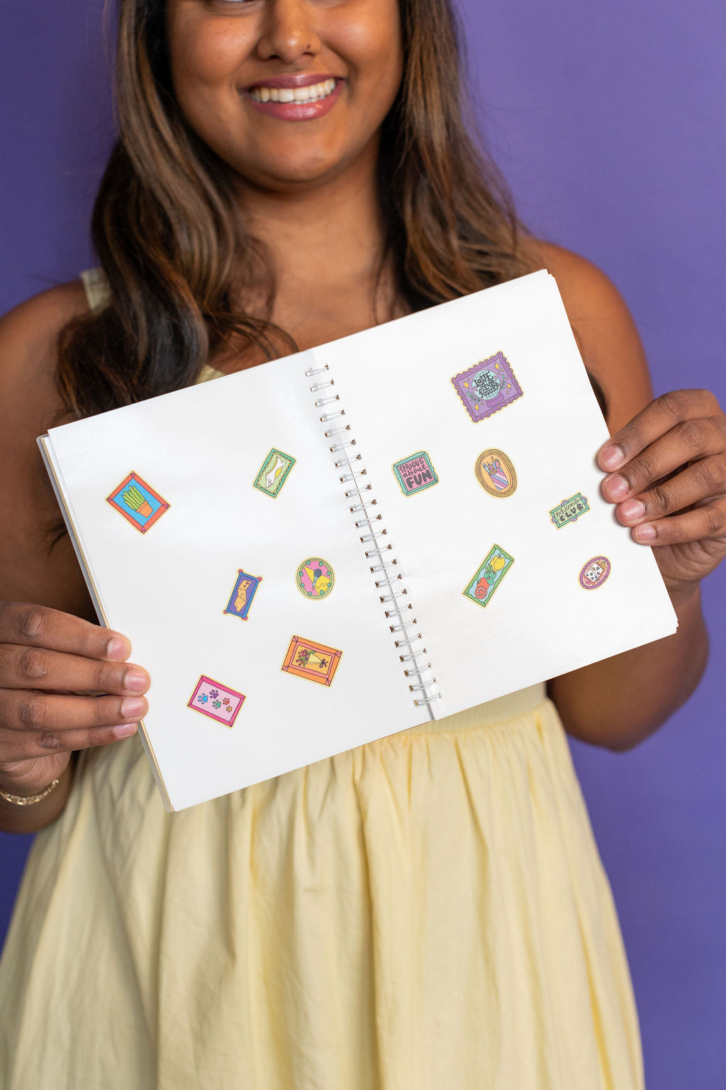 Woman holding a sticker book with colorful stickers on a purple background