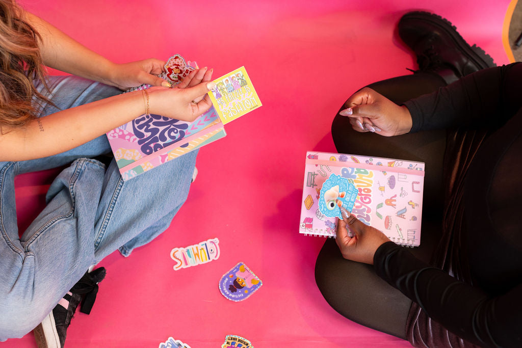 Two people sitting on a pink floor playing with colorful cards.