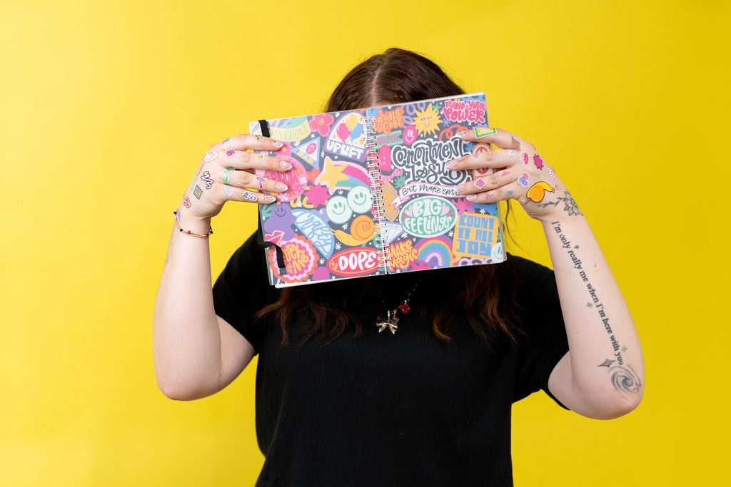 Person holding a colorful sticker book with text and graphics against a yellow background