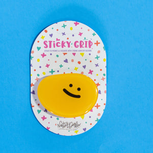 Yellow smiley face sticker on a blue background with colorful 'Sticky Grip' packaging.