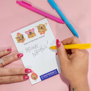Person holding a yellow pen over a piece of paper with stickers and text on a pink background