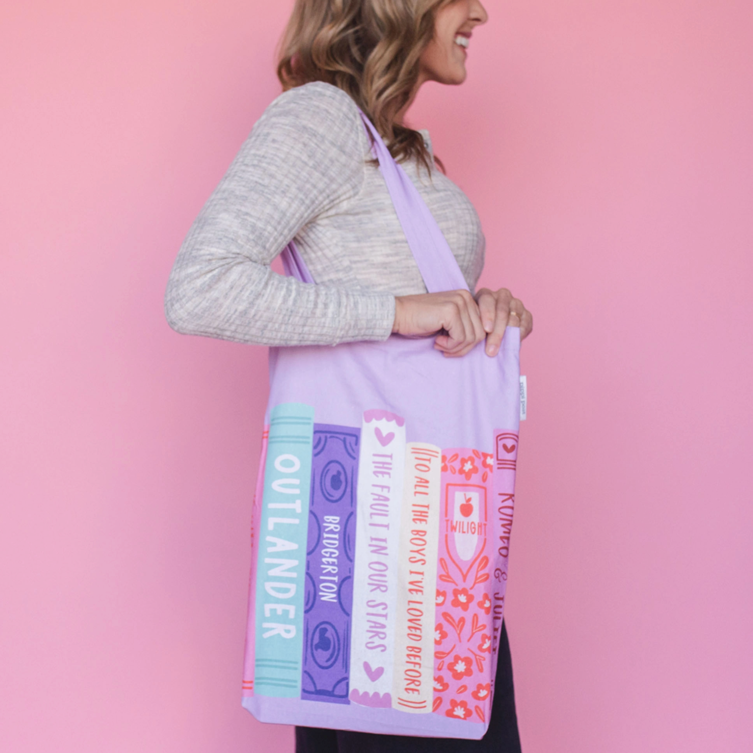 Woman wearing a colorful book-themed tote bag against a pink background