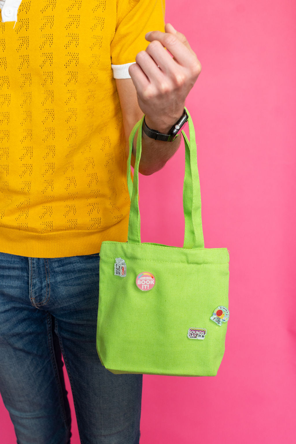 Person holding a green bag with logos against a pink background