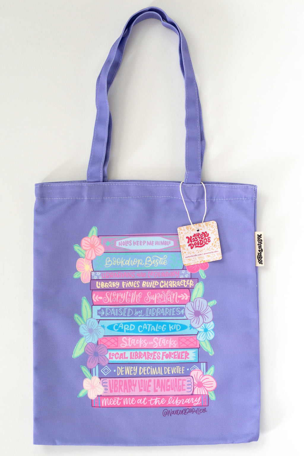 Purple tote bag with colorful text and floral designs on a white background