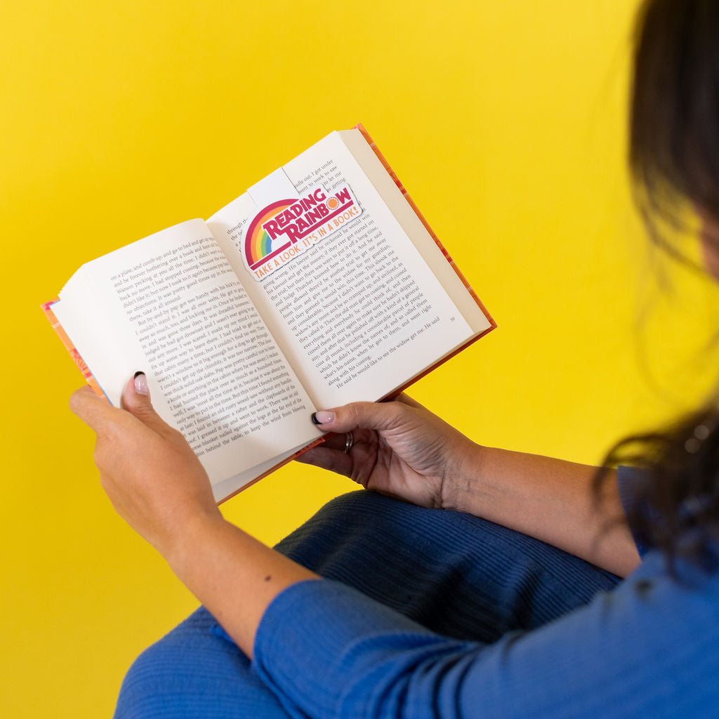 Person reading a book with a colorful cover against a yellow background