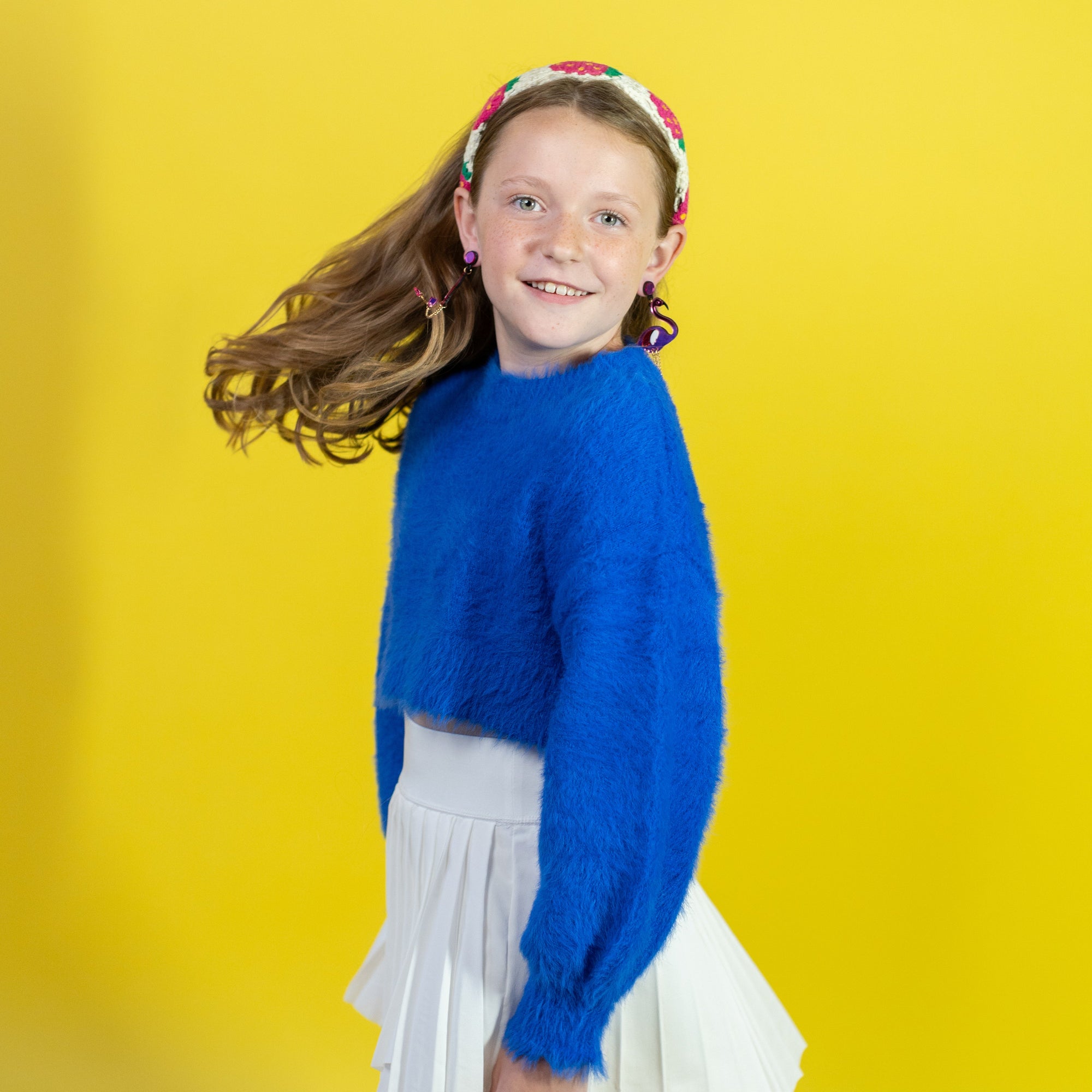 Young girl in a blue sweater and white skirt with a colorful headband against a yellow background