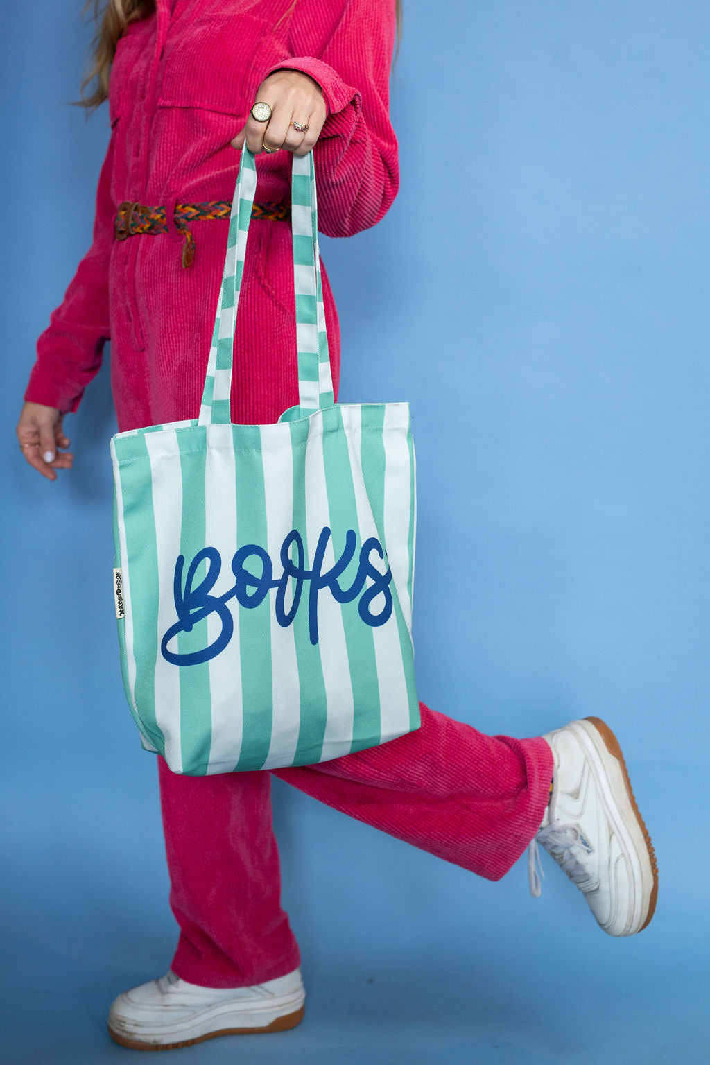 Person holding a green and white striped tote bag with 'BOOKS' written on it against a blue background