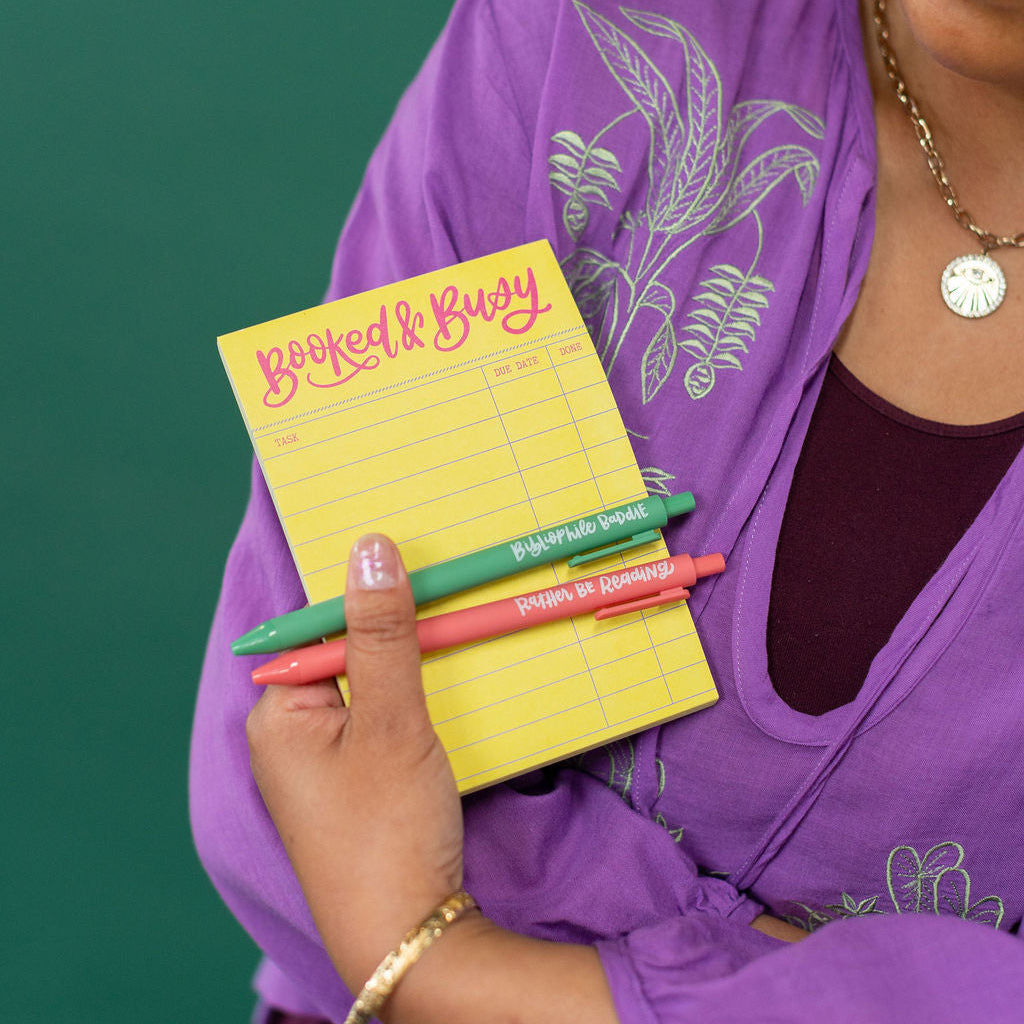 Person holding a yellow notepad with colorful pens against a green background