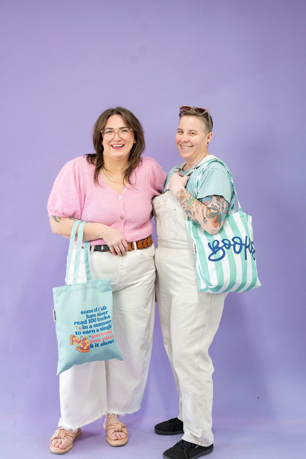Two people holding tote bags with text against a purple background