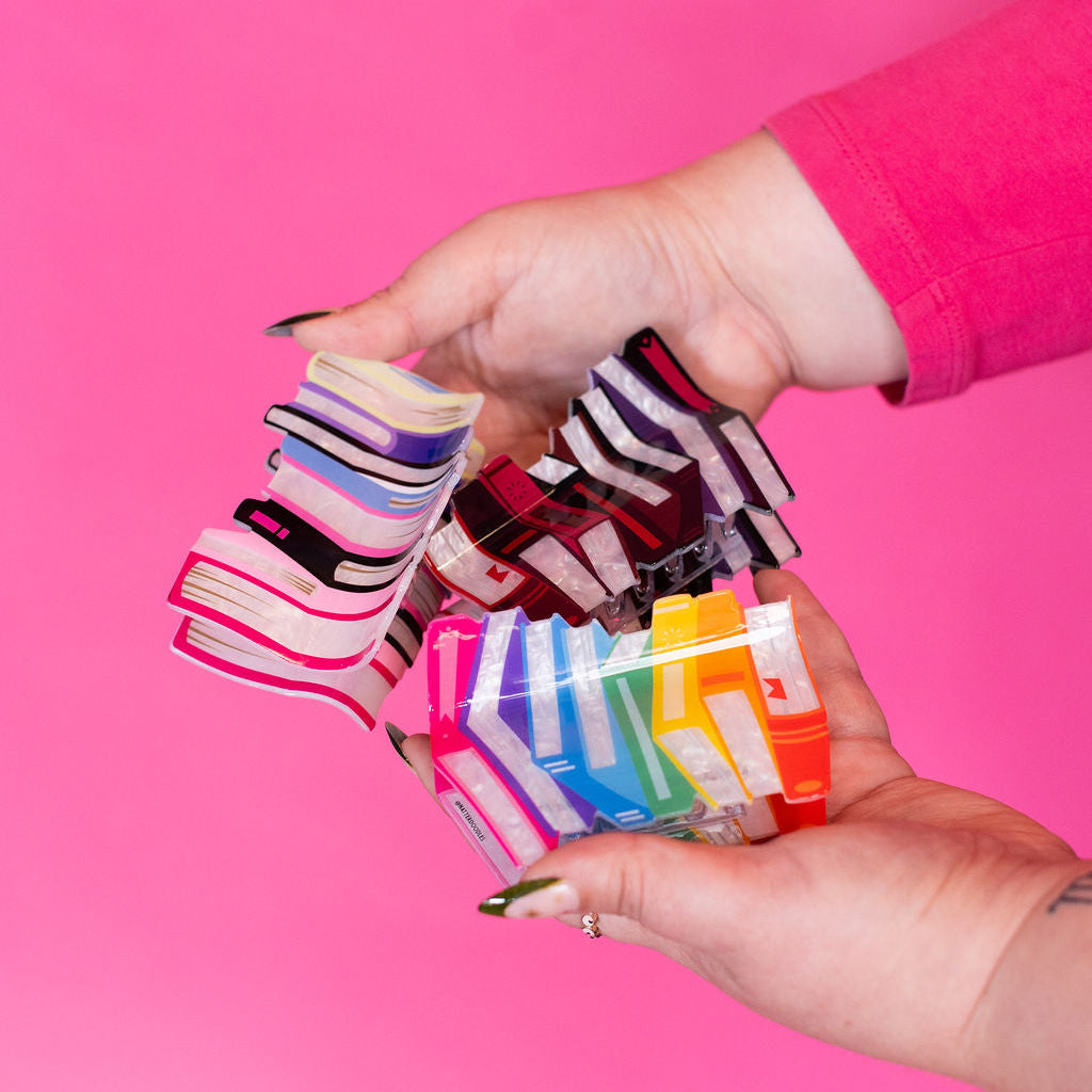 Colorful hair clips held by a person against a pink background