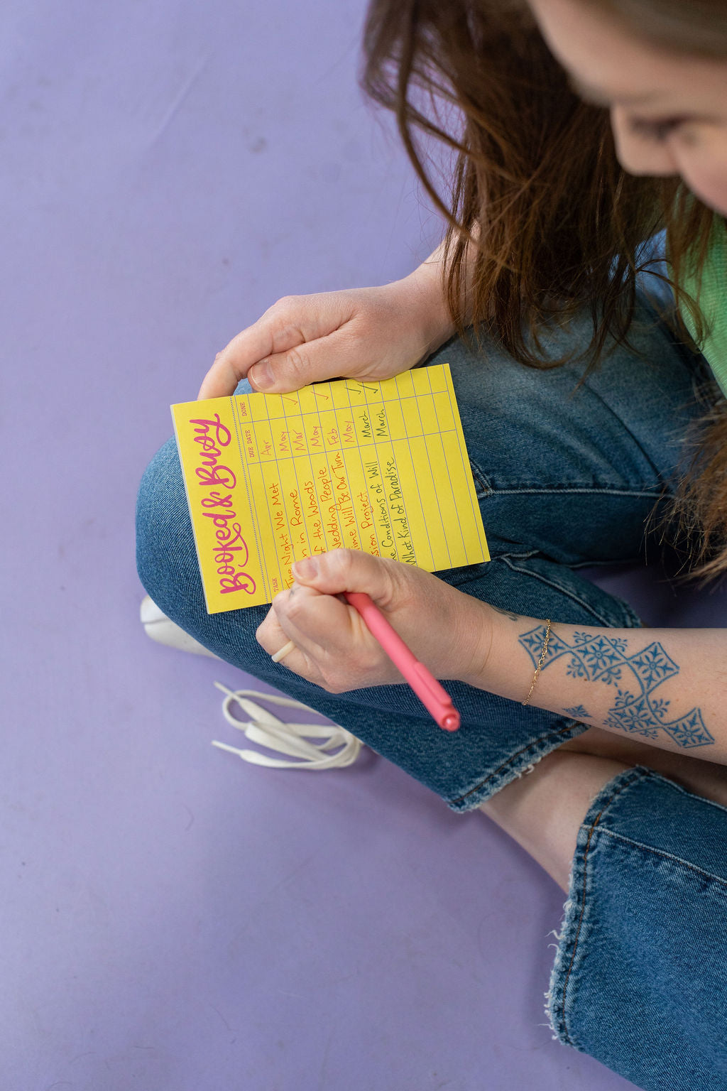 Person holding a yellow notepad and pink pen on a purple background