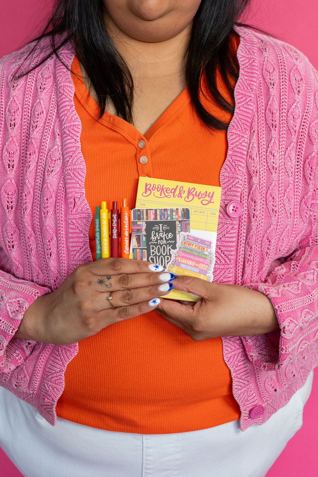 Person holding a book and colorful markers against a pink background