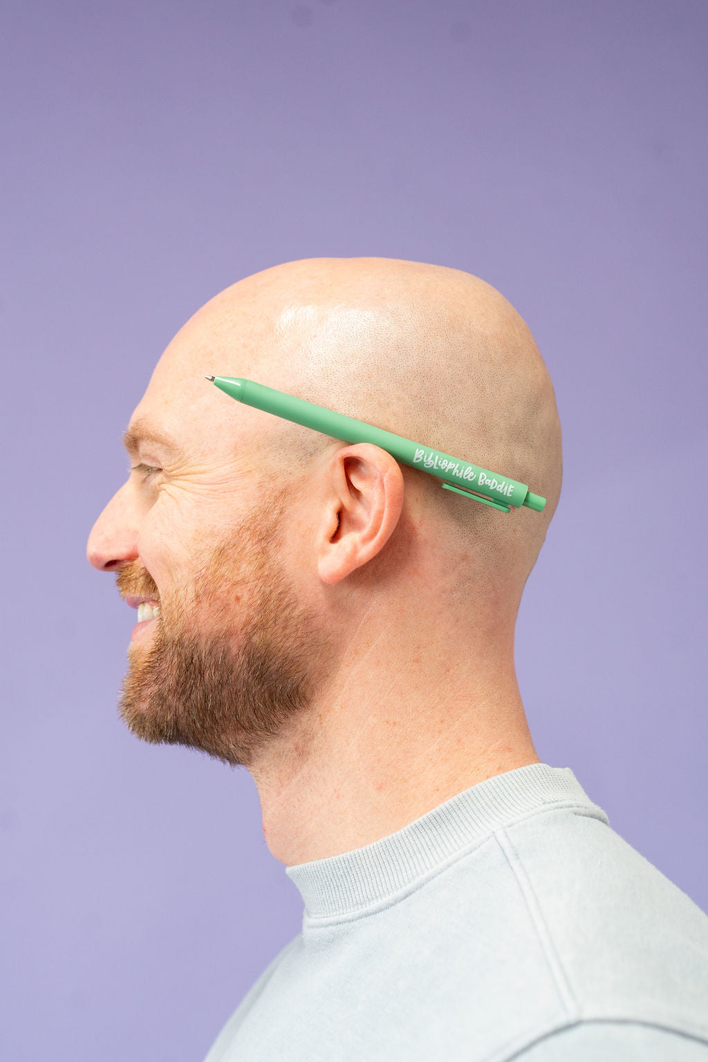 Man with a green pen on his head against a purple background