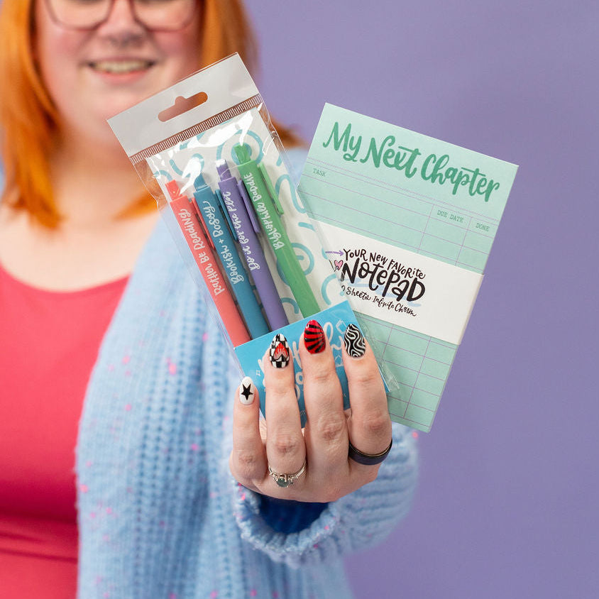 Person holding stationery items including pens and a notebook against a purple background