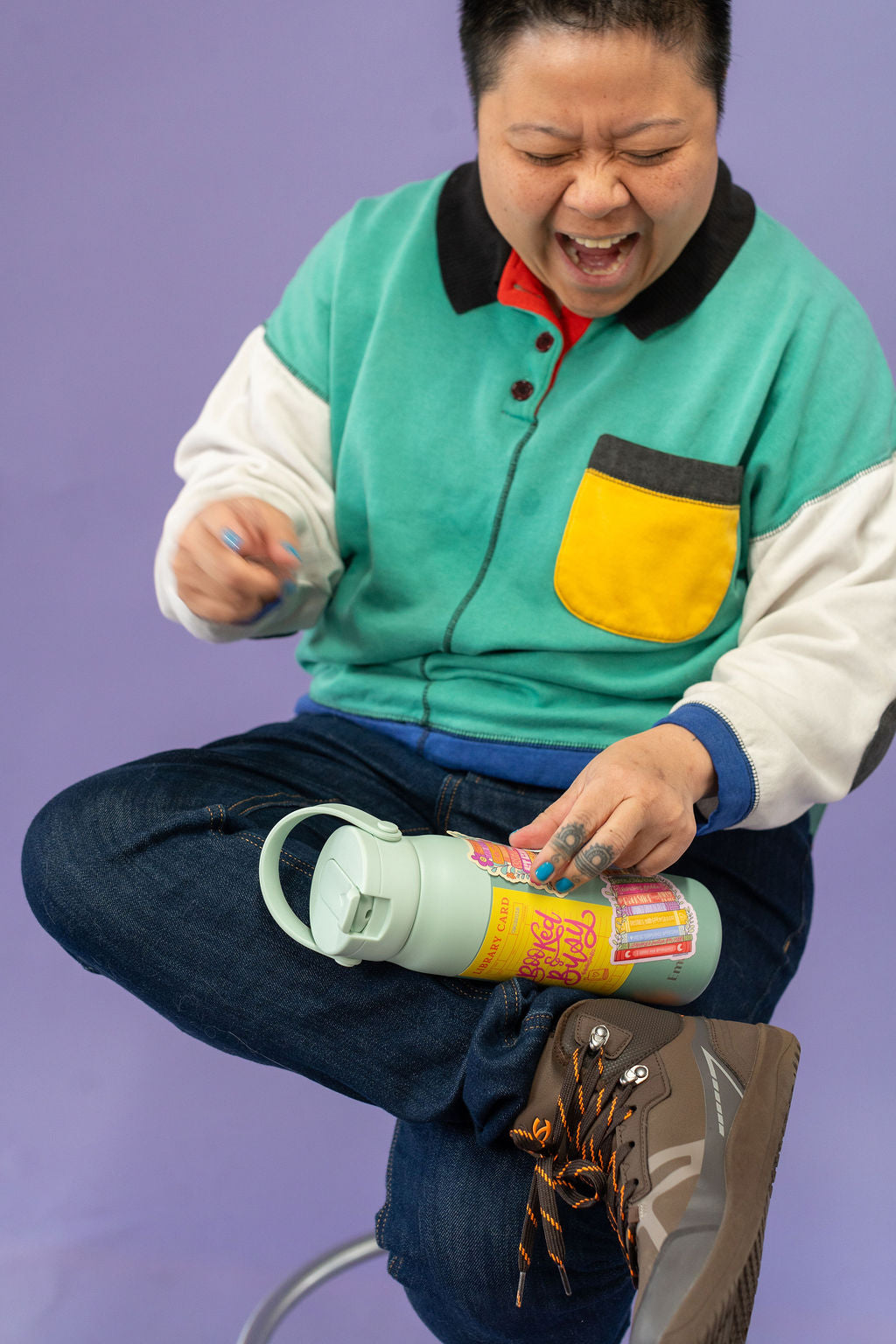 Person holding a water bottle with colorful stickers against a purple background