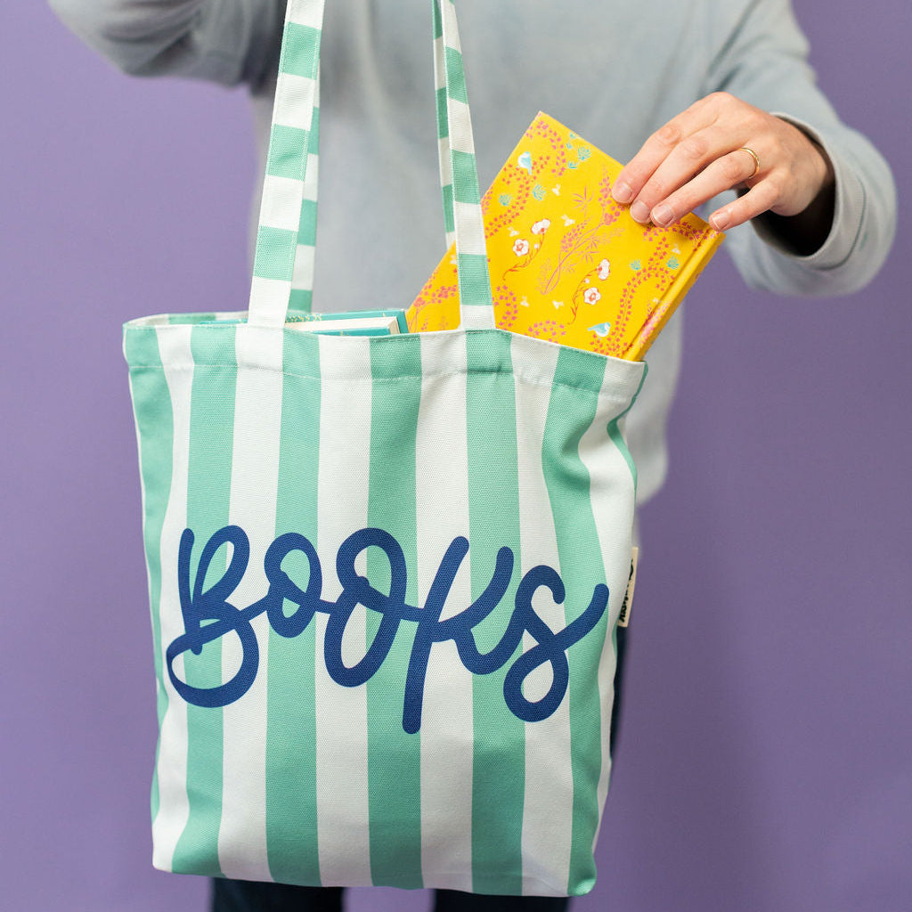 Person holding a striped tote bag with 'books' written on it against a purple background