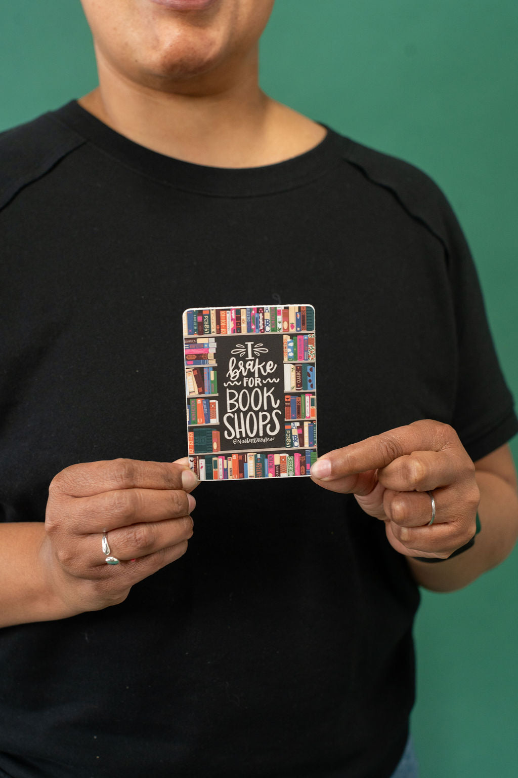 Person holding a colorful sticker with text against a green background
