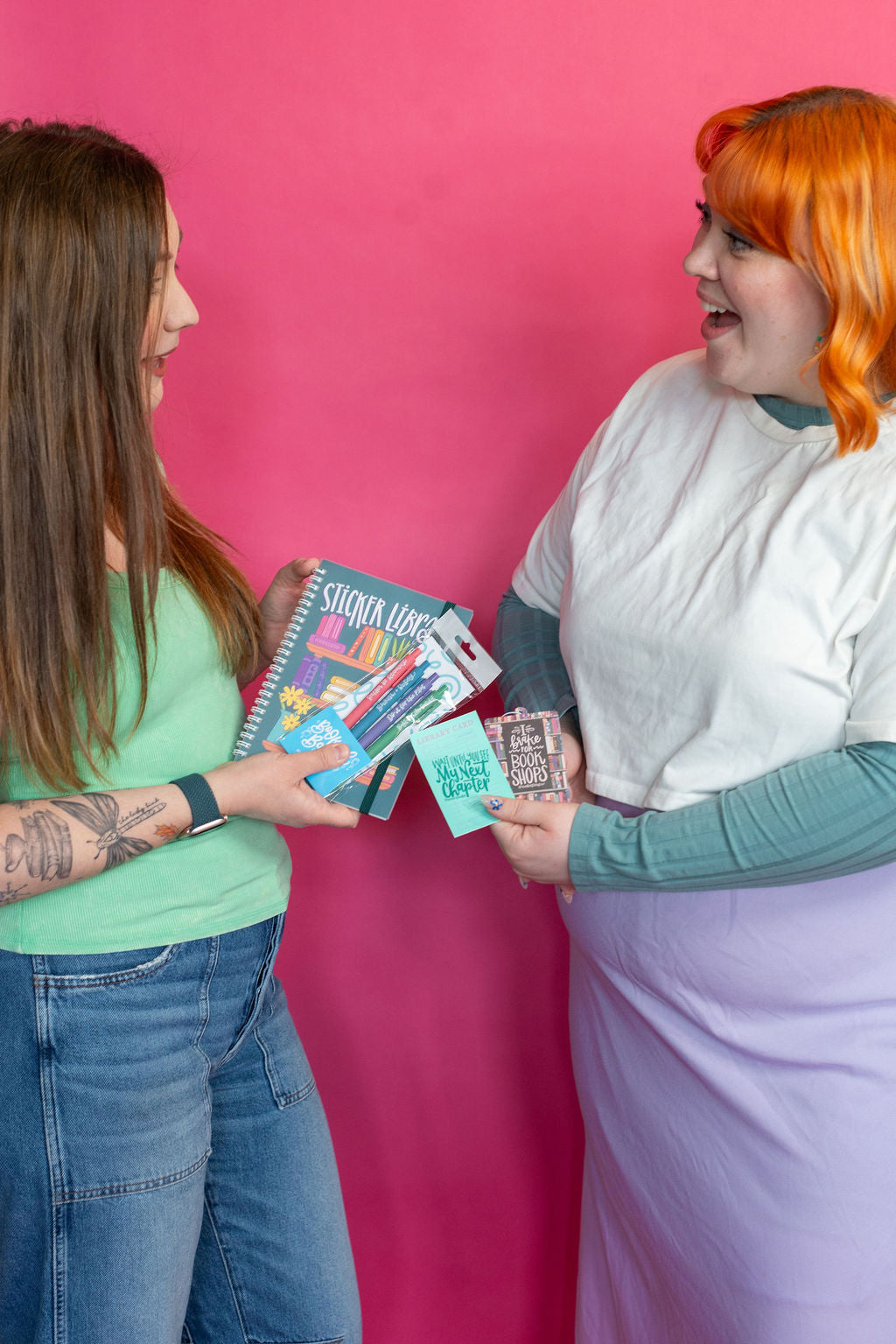 Two women interacting with colorful  stationery items against a pink background