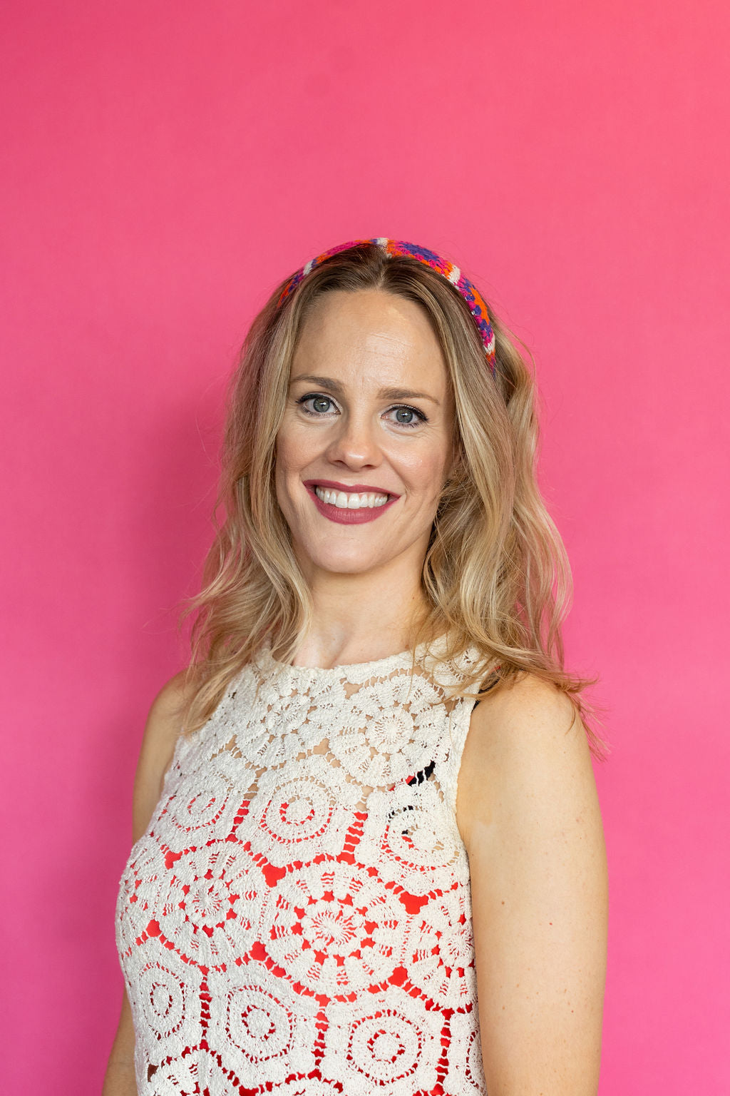 Woman wearing a white lace dress with red patterns against a pink background