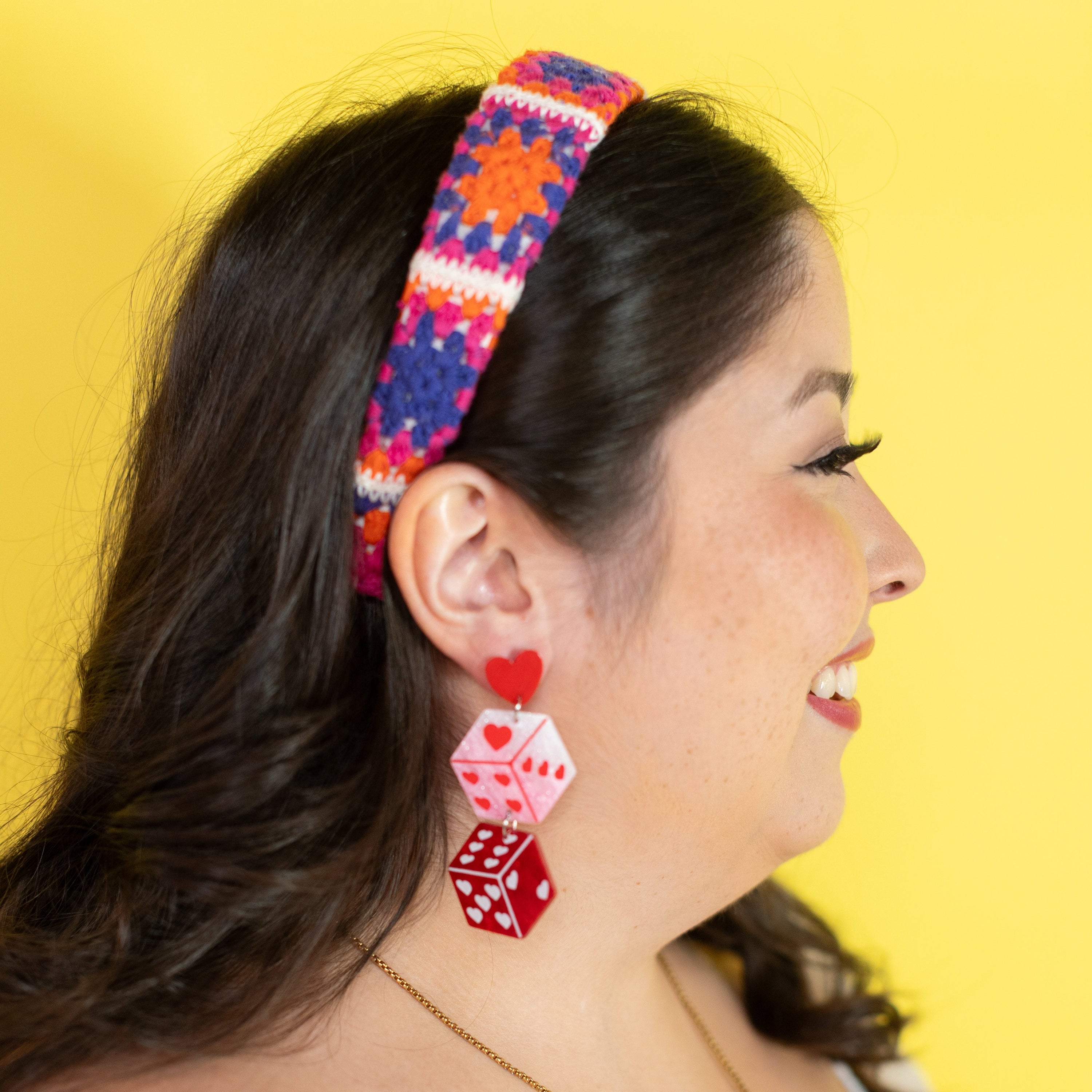 Woman wearing colorful headband and red dice-shaped earrings against a yellow background
