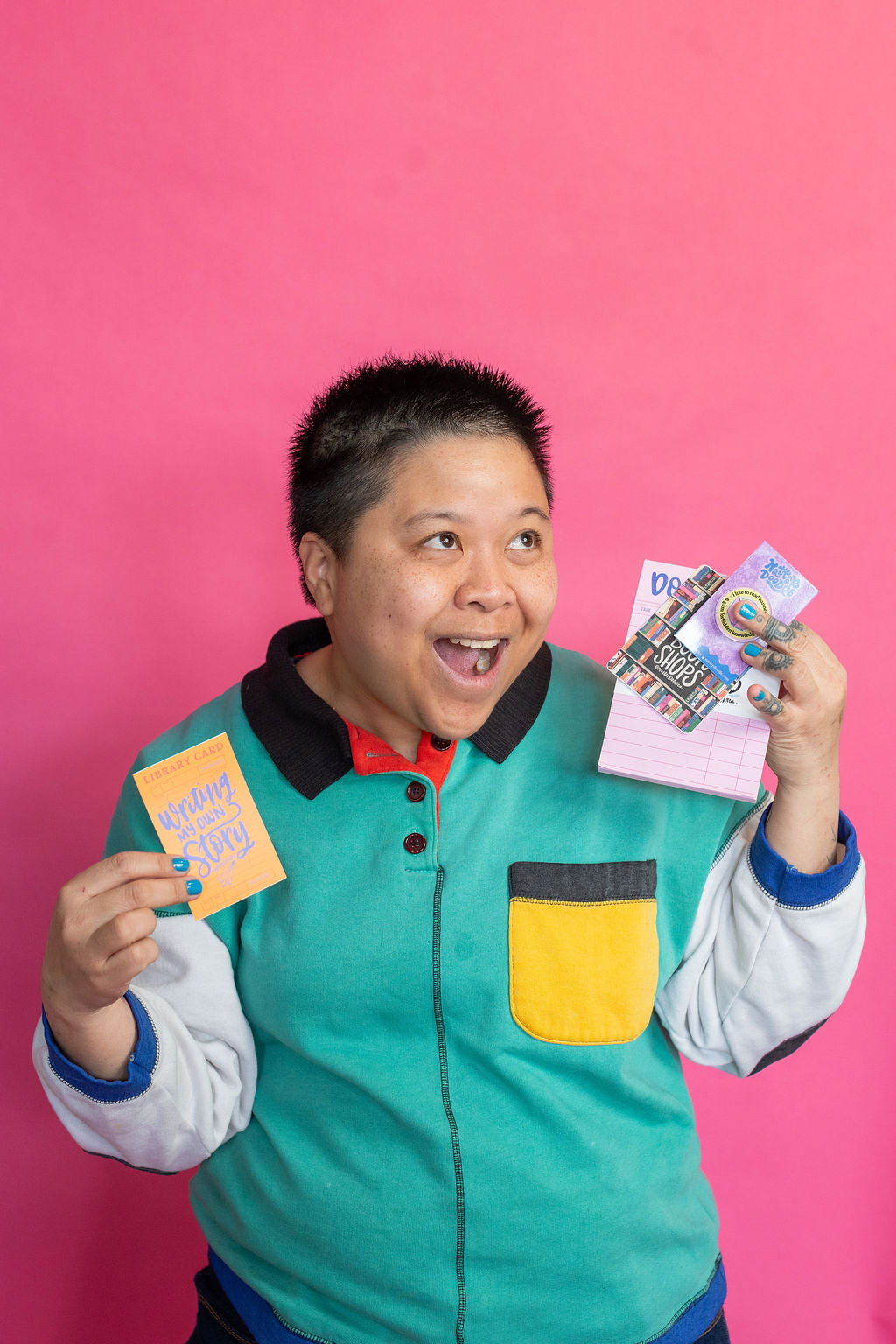 Person holding colorful bookish stationery against a pink background