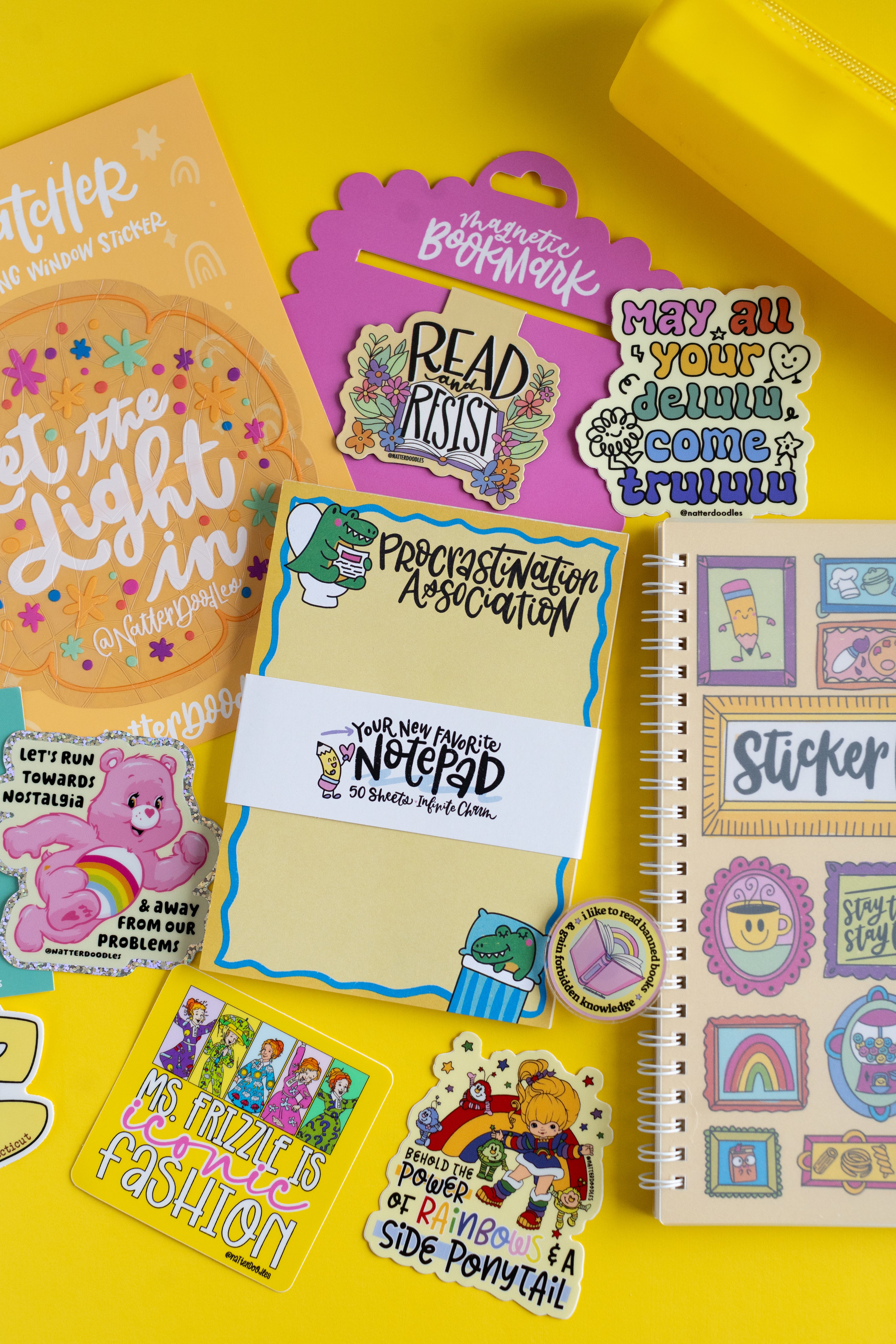 Collection of colorful stationery items including a notebook, stickers, and a bookmark on a yellow background.