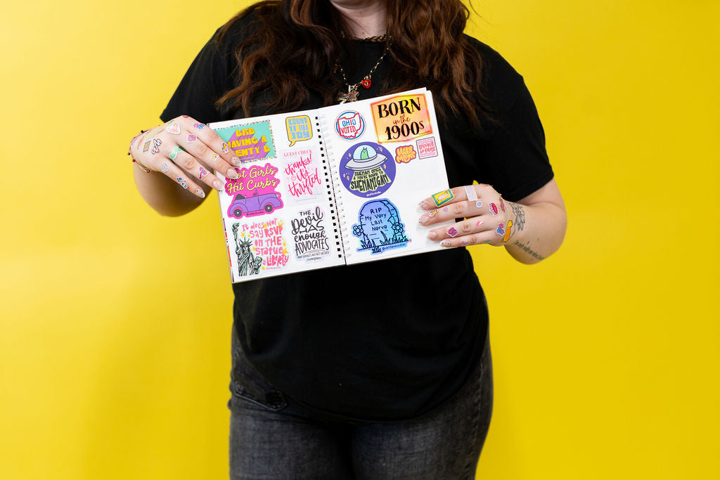 Person holding a notebook with colorful stickers against a yellow background