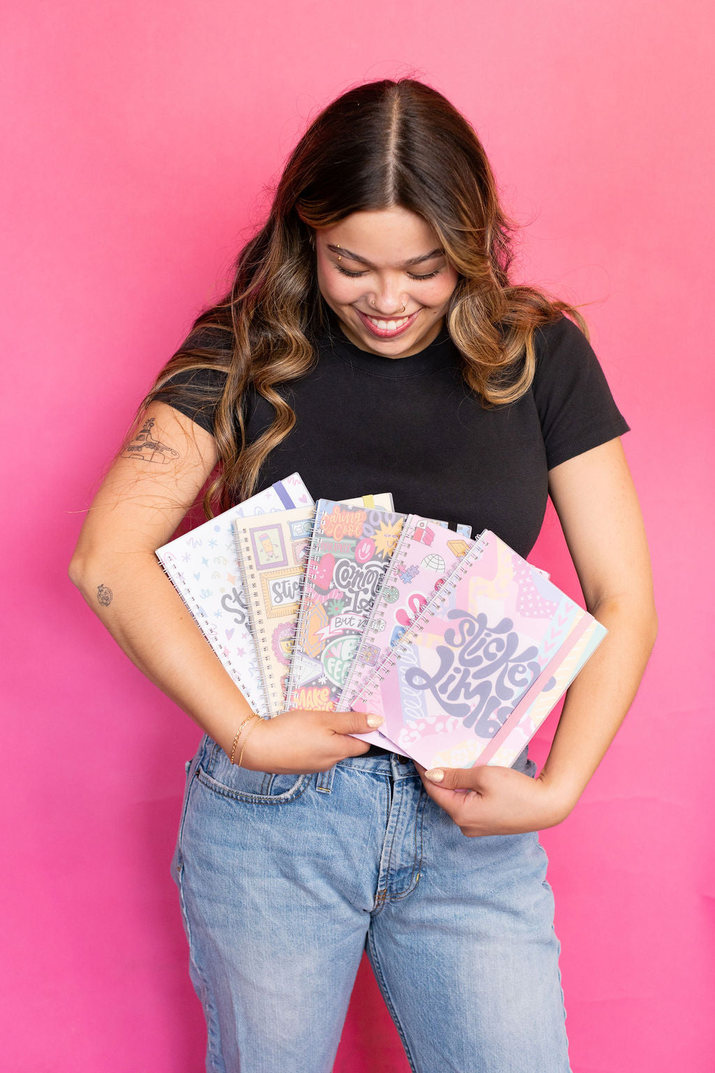 Woman holding colorful sticker books against a pink background