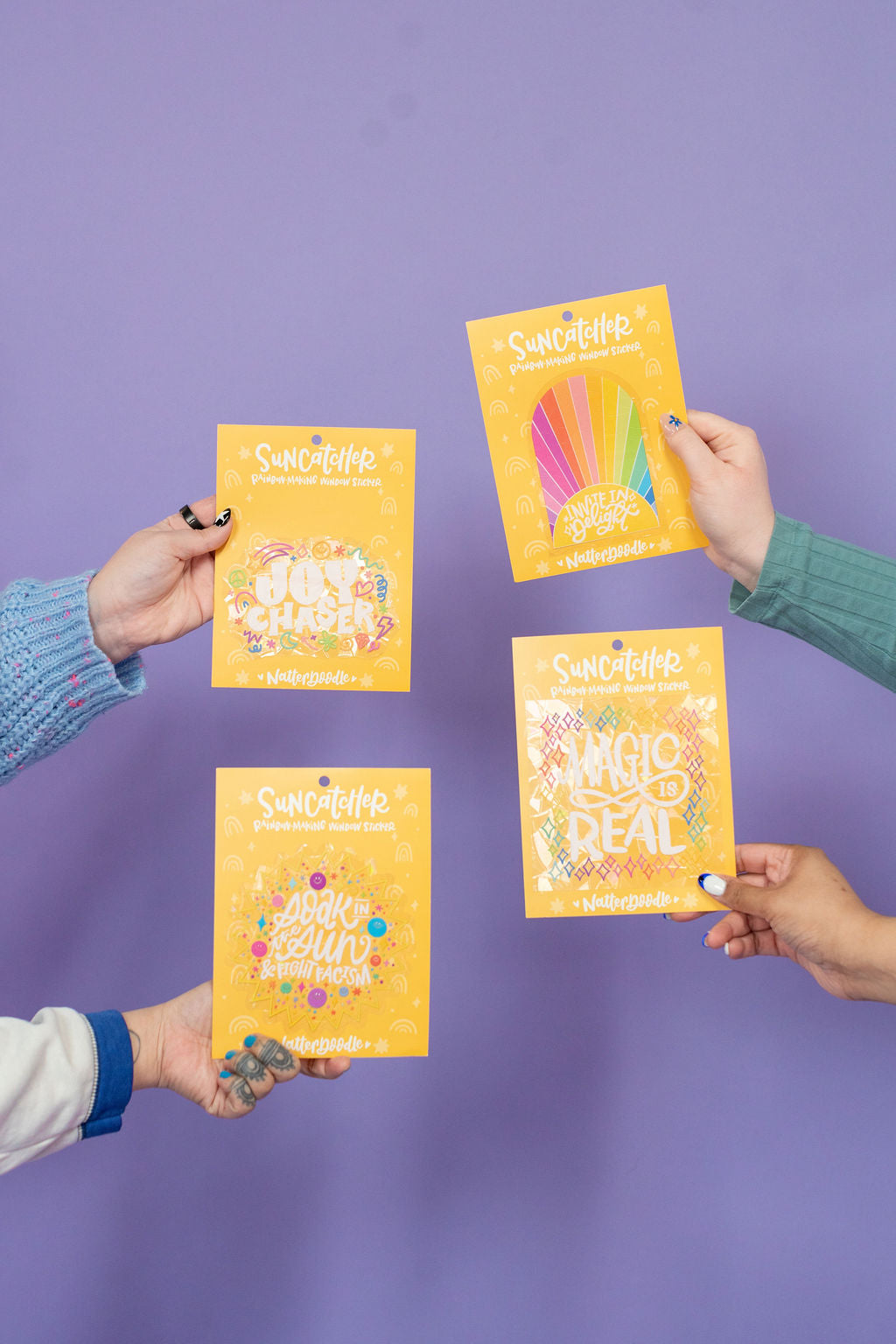 Four hands holding yellow packages with colorful designs against a purple background