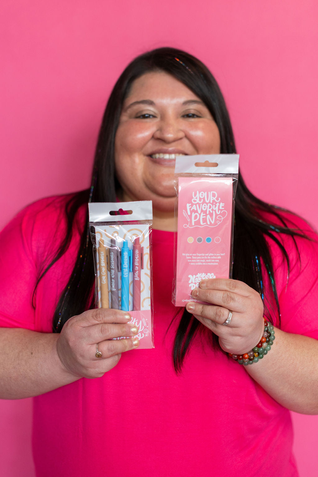 Person holding pen products against a pink background