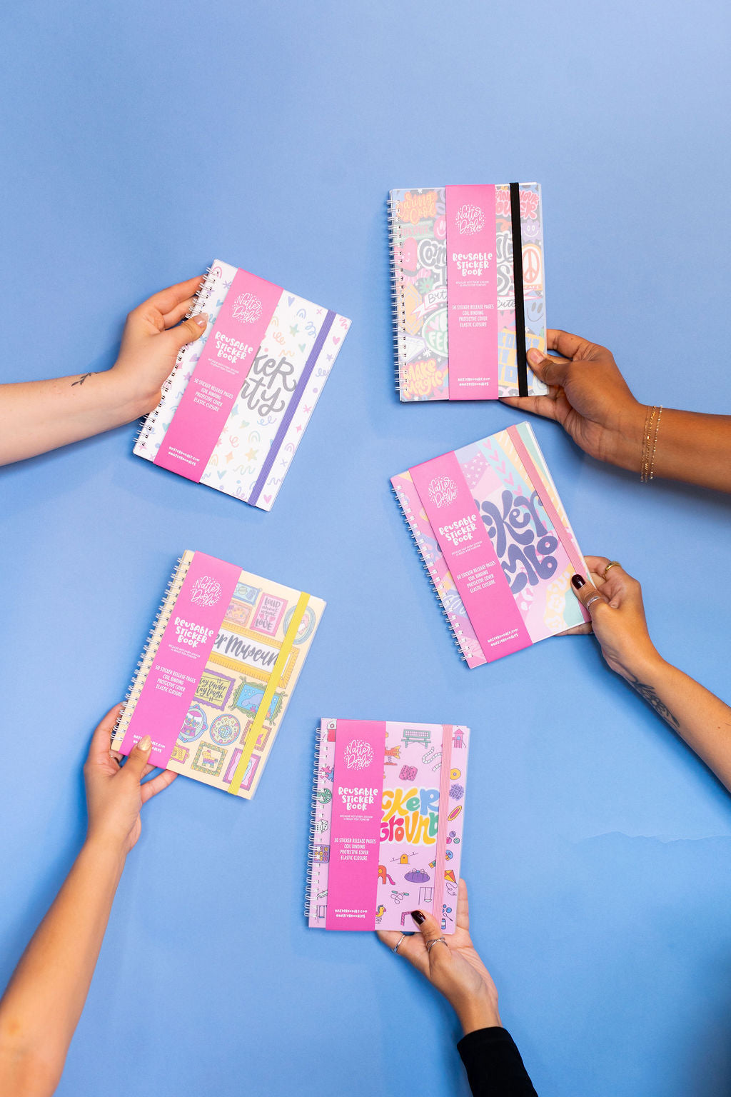 Five colorful sticker books held by hands on a blue background