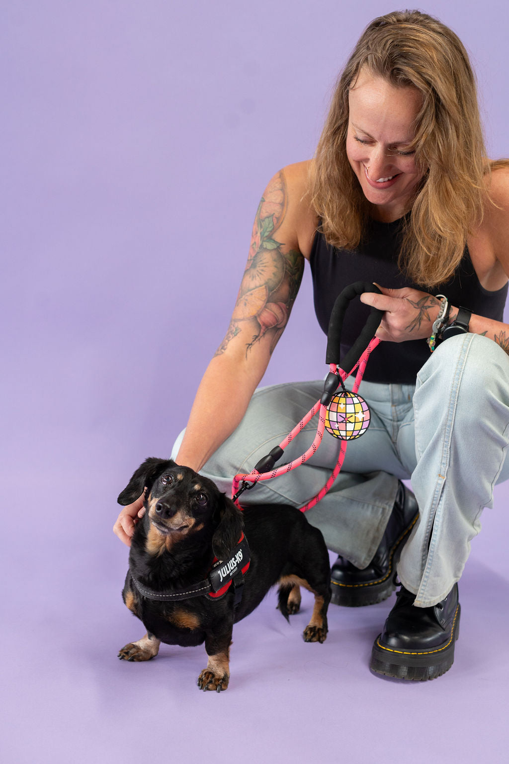 Woman with tattoos and a dog on a leash against a purple background