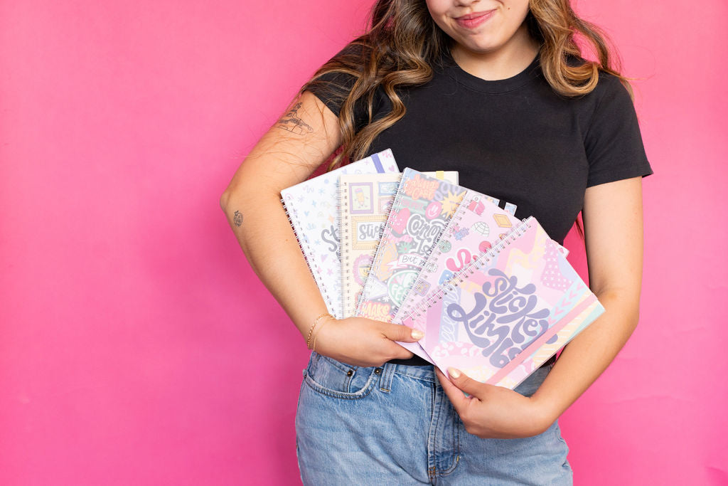 Person holding colorful notebooks against a pink background