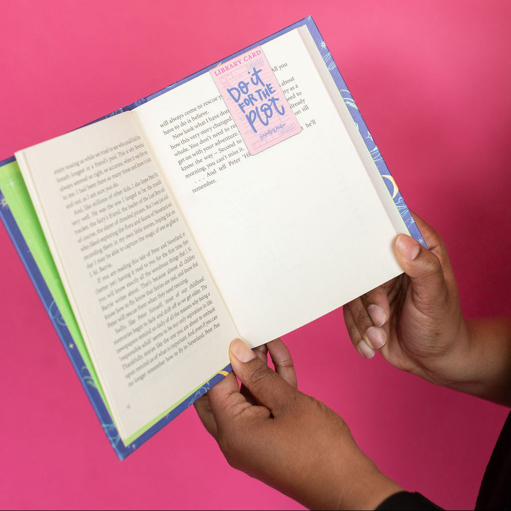 Open book held by hands against a pink background