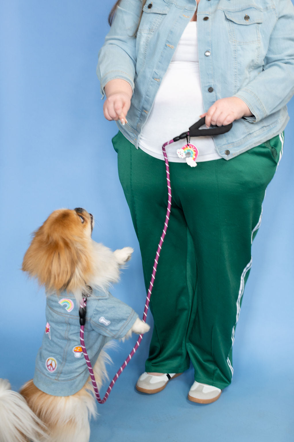 Person in green pants and denim jacket with a dog on a blue background